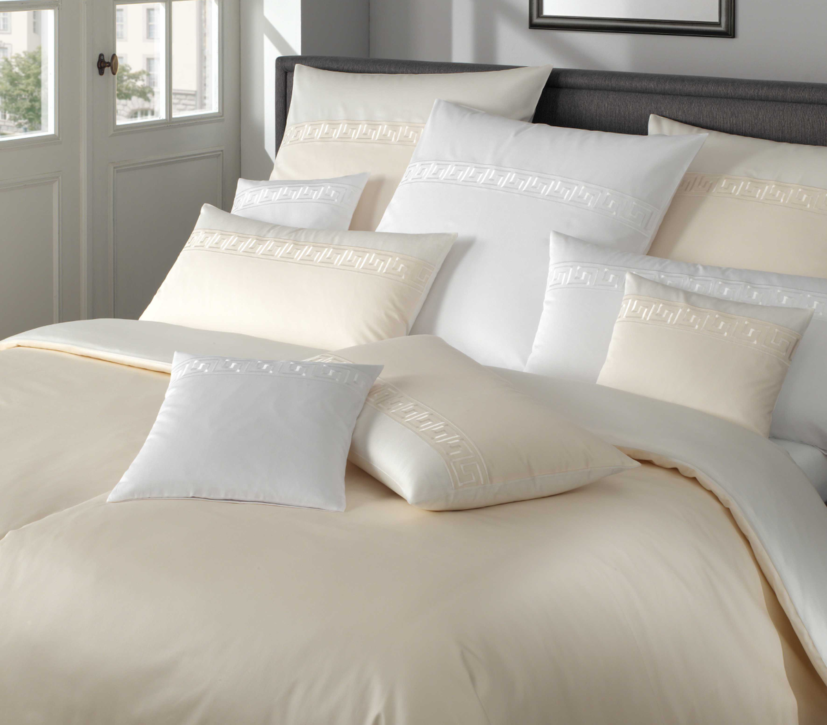 Neatly arranged pillows on a bed with a neutral color scheme and Greek patterns.