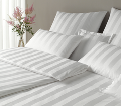 Gray and white striped bedding set on a bed with a vase of flowers in the background.