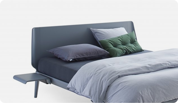 Modern bed with gray bedding and green pillow on a white background with a side table