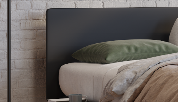 Bed with green pillow and beige blanket against a stone wall
