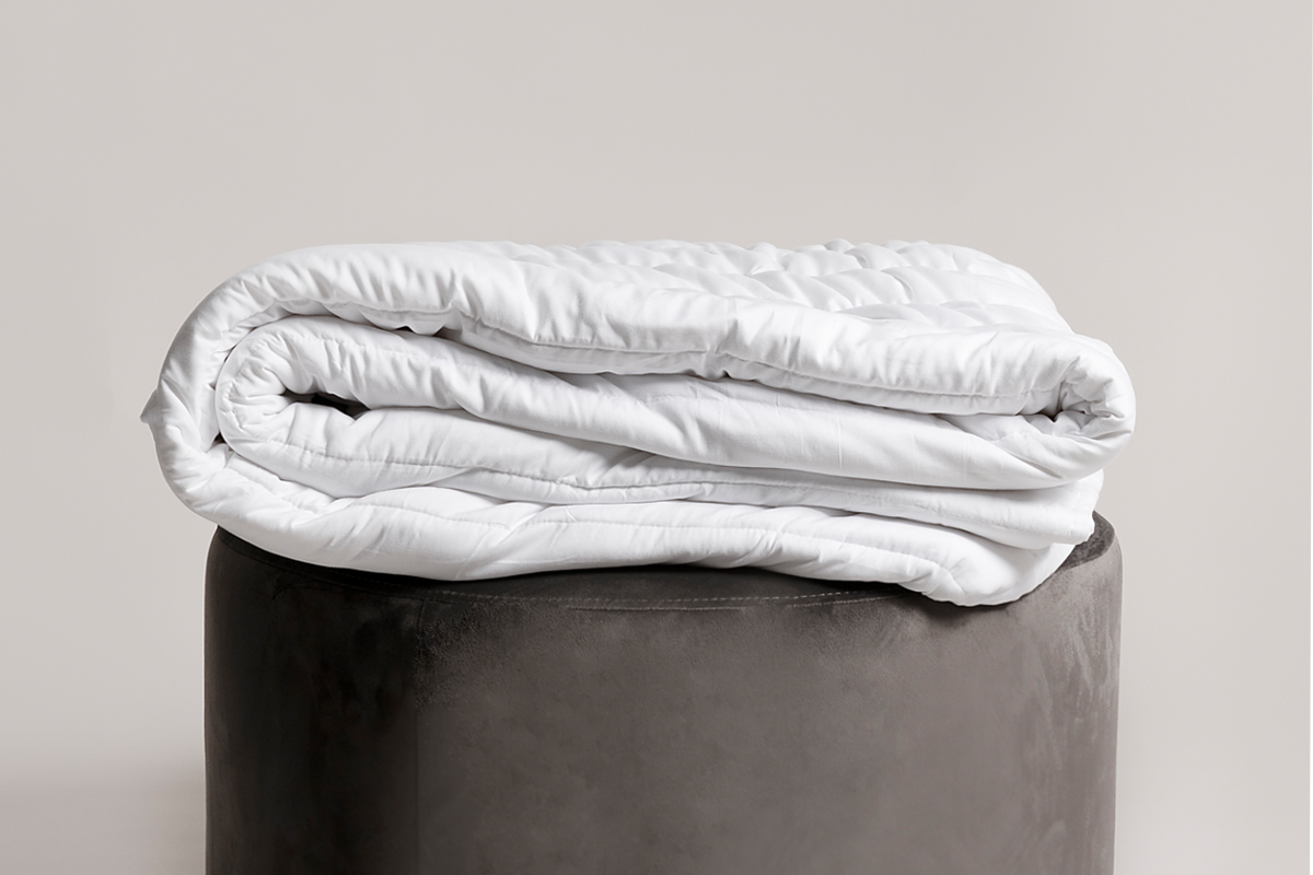 White comforter on a gray ottoman against a plain background