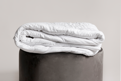 White comforter on a gray ottoman against a plain background