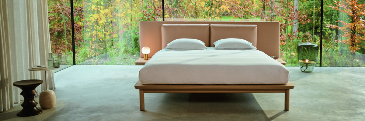 Modern bedroom with a large Auping Noble bed and large windows overlooking a forest.