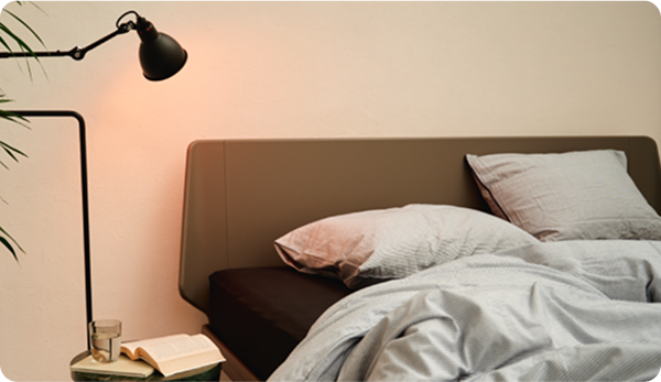 Bedroom scene with a bed, lamp, and book on a nightstand.