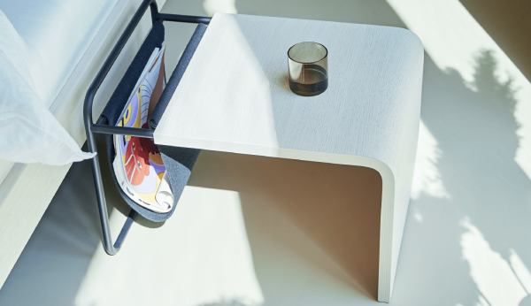 Small white table with a magazine and candle on a light background