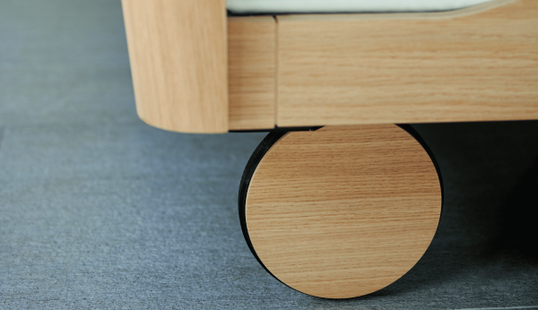 Close-up of a wooden bed wheel legs on a gray carpet.