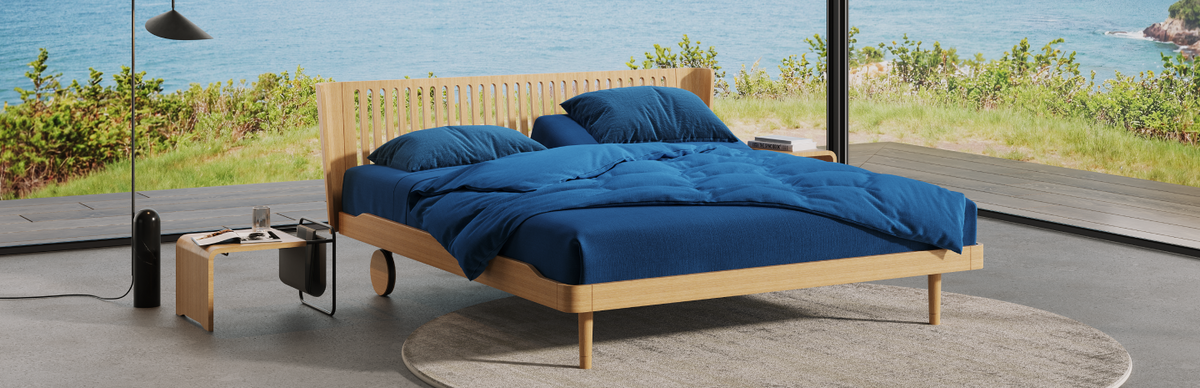 Wooden bed with blue bedding in a modern room with a view of water and greenery.