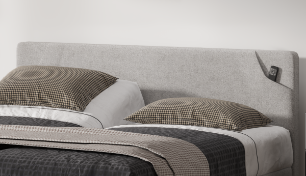 Gray upholstered bed with plaid pillows and a blanket on a white background
